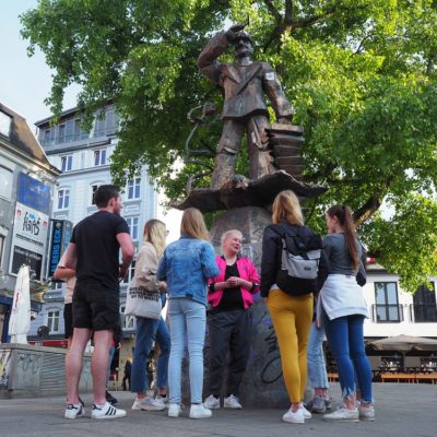 Die Schülergruppe macht während des Stadtteilrundgangs halt auf dem Hans-Albers-Platz. Von Tourguide Dani erfahren die Schüler*innen viel über die Geschichte des Platzes und das alltägliche Leben auf St. Pauli.